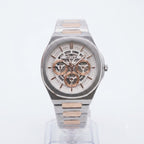 A two-tone stainless steel and rose gold wristwatch with a complex skeleton dial, displayed on a clear stand against a white background.