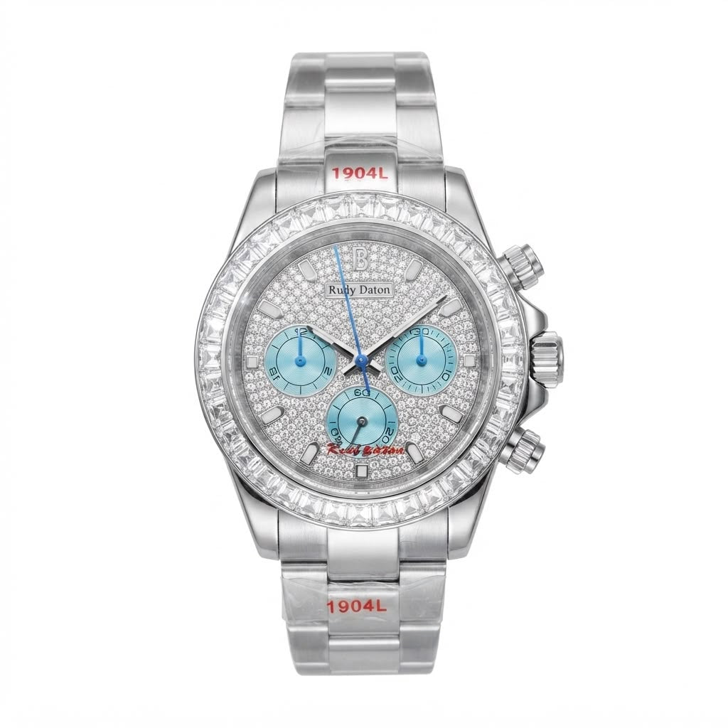 A silver stainless steel wristwatch with a diamond-encrusted bezel, a silver dial covered in small diamonds, and three light blue chronograph sub-dials. The brand name 'Kelly Dutton' is visible on the dial, and '1904L' is printed in red on the bracelet links.