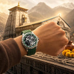 A wrist wearing a green rubber strap watch with a silver-tone case and skeleton dial, posed in front of a temple and mountains.
