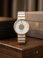 A Time Square ceramic watch with a white dial and white rectangular ceramic links, accented by a gold-tone case and central dial detail, displayed on a wooden surface with its branded box in the background.