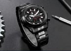 A black stainless steel wristwatch with a black dial, silver-tone hands and markers, and a thin red seconds hand. The watch is displayed on a dark textured surface with a gear on the left and a screwdriver on the right.