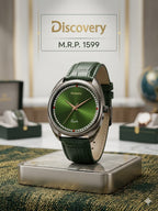 A Discovery wristwatch with a green dial and dark green leather strap, displayed on a metallic stand. The watch is set against a softly blurred background with a watch box and a globe, and a text overlay at the top reads 'Discovery M.