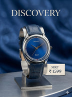 A wristwatch with a blue leather strap and a blue dial, displayed on a metal stand against a dark blue draped background. The brand name 'Discovery' is printed at the top, and a label at the bottom right reads 'MRP ₽1599'.