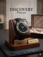 A wristwatch with a black leather strap and black dial displayed on a wooden stand. The watch face shows the brands Discovery and Cook.