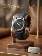 Discovery brand wristwatch with a dark blue leather strap and a black dial, displayed on a wooden stand. The watch is set against a warm, blurred background with a leather bag and gold-toned accents.