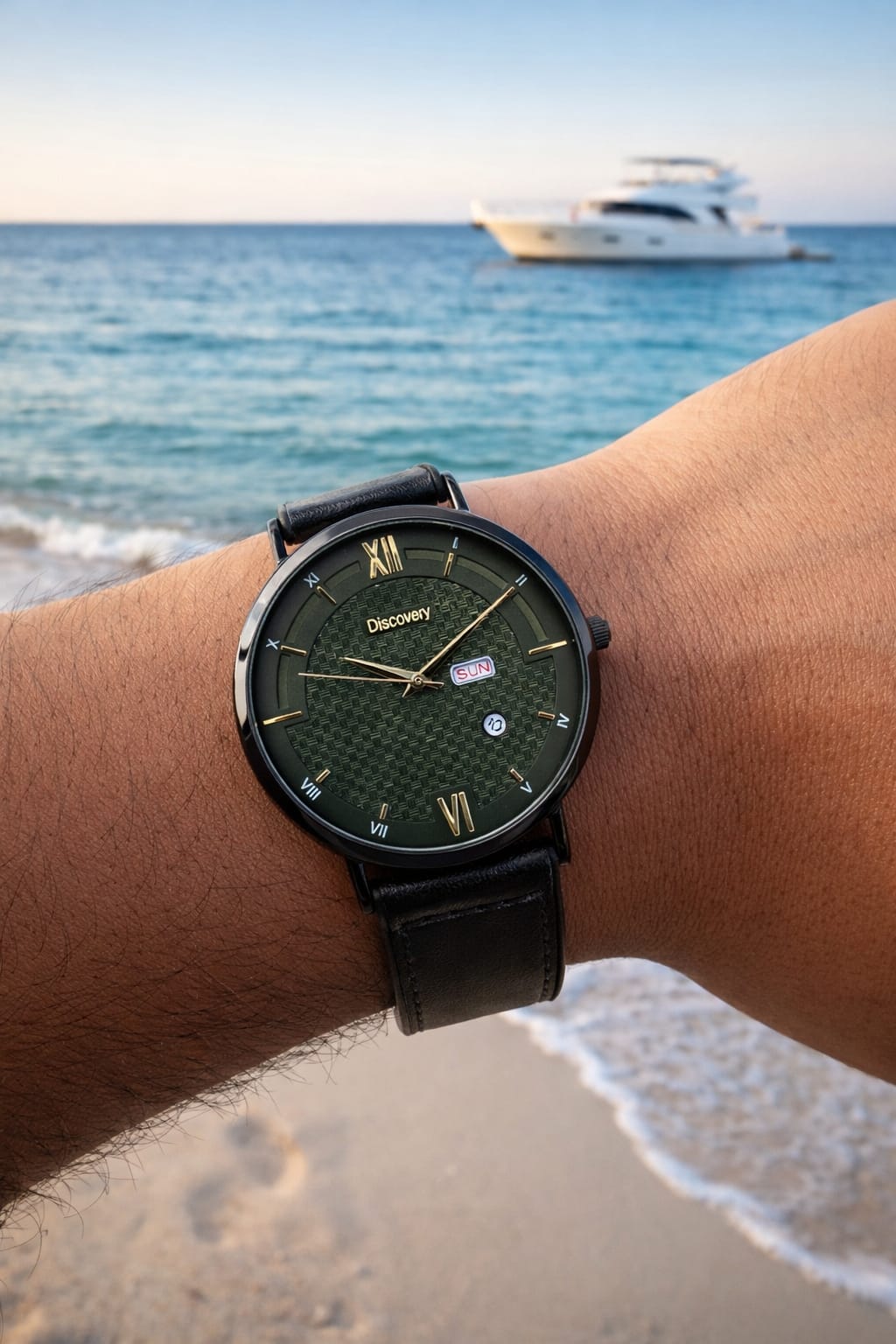 A wristwatch with a dark green textured dial and black leather strap worn on a person's wrist, with a beach and ocean in the background and a white yacht on the horizon.