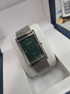 A silver-tone rectangular analog watch with a textured dark green dial and a matching silver mesh strap, displayed inside a white watch box.