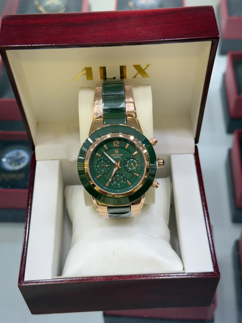 A green dial and green ceramic-link wristwatch with a rose gold case, presented inside an open dark red ALIX gift box with a white cushion.