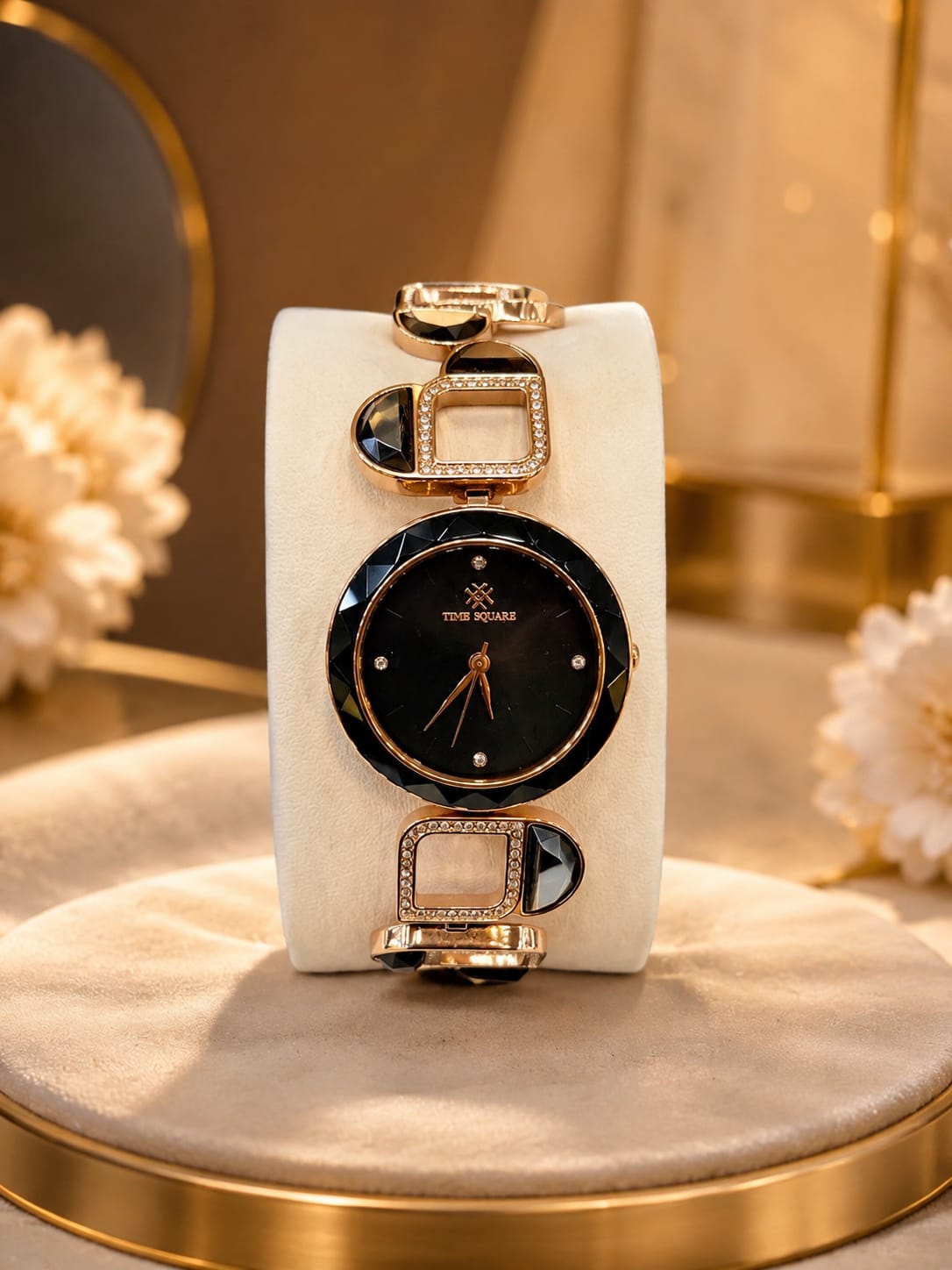 A gold-tone and black watch with a round black dial and rhinestone accents, displayed on a white cushion atop a gold pedestal in a warm, elegant setting.