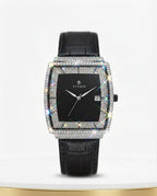 A rectangular women's watch with a black dial, a bezel paved with small clear stones, and a black leather strap, shown on a white background with a gold base.