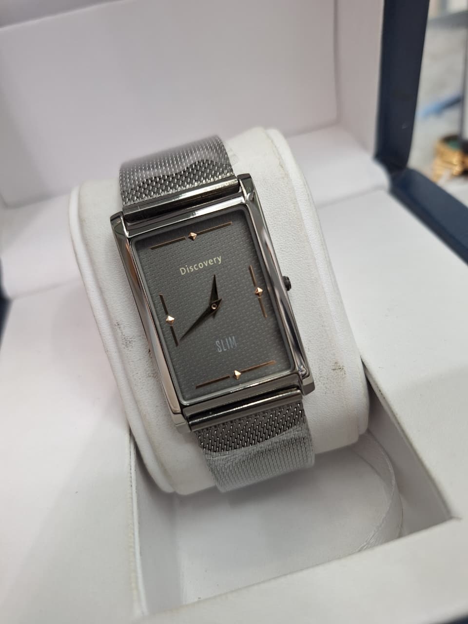 A Discovery SLUM women's watch with a silver-tone rectangular case, textured dark gray dial, and matching silver mesh strap, displayed inside its white presentation box.